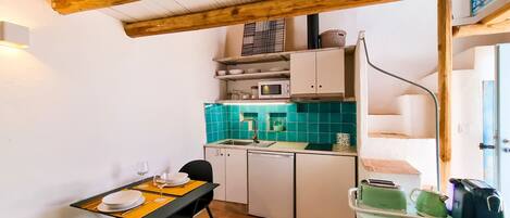 Cocina compacta con microondas, lavabo y armarios. Hay una mesa de comedor con sillas y una lámpara de mesa pequeña.