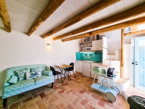 Une pièce chaleureuse avec un canapé à motifs, une petite table à manger, un coin cuisine équipé d’un four à micro-ondes et une porte bleue.