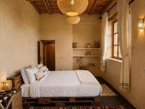 A bedroom with a wooden bed, white bedding, a woven light fixture, and a window with curtains. - Family Farm House with Animals near Essaouira and Kaouki Beach (Essaouira)