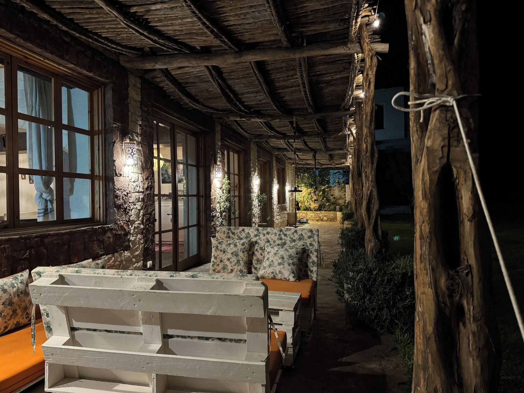 A rustic outdoor seating area with wooden benches and tables, surrounded by stone walls and vegetation.