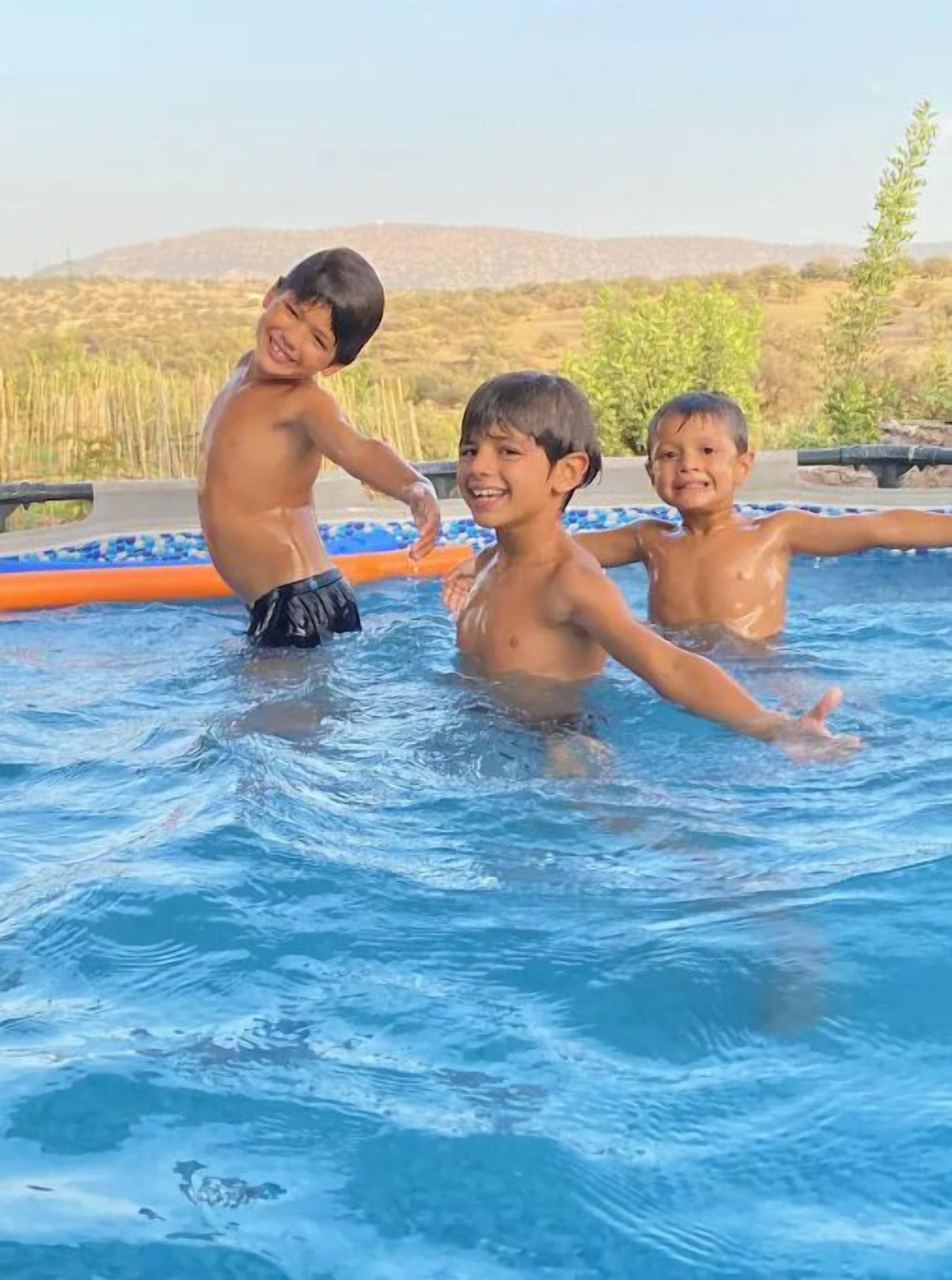 Drei Kinder spielen in einem Schwimmbecken mit Blick auf Hügel im Hintergrund.