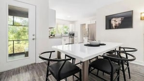 A modern dining area with a white table and black chairs, a kitchen in the background, and a framed artwork on the wall. - 3,700 sqft-Cozy/Private Villa style Ranch in SouthPark-King en Suite-Winter Rdy! (Charlotte)