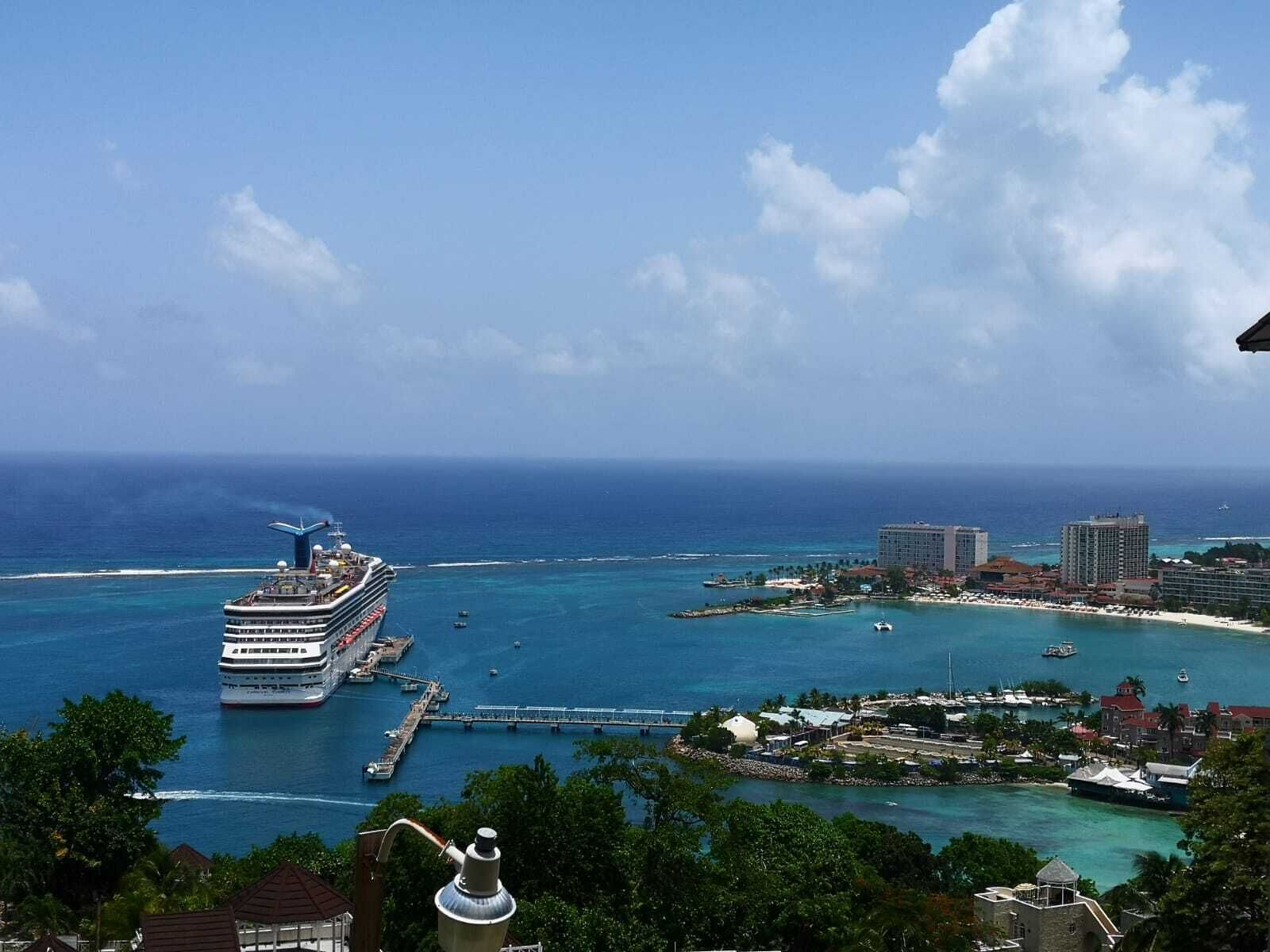 A cruise ship docked at a port with a view of the ocean and nearby buildings.