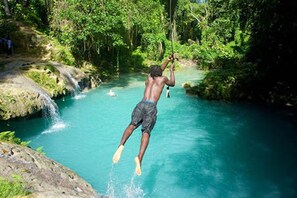 Une personne sautant dans une rivière aux eaux d’un bleu limpide, entourée d’une végétation luxuriante.