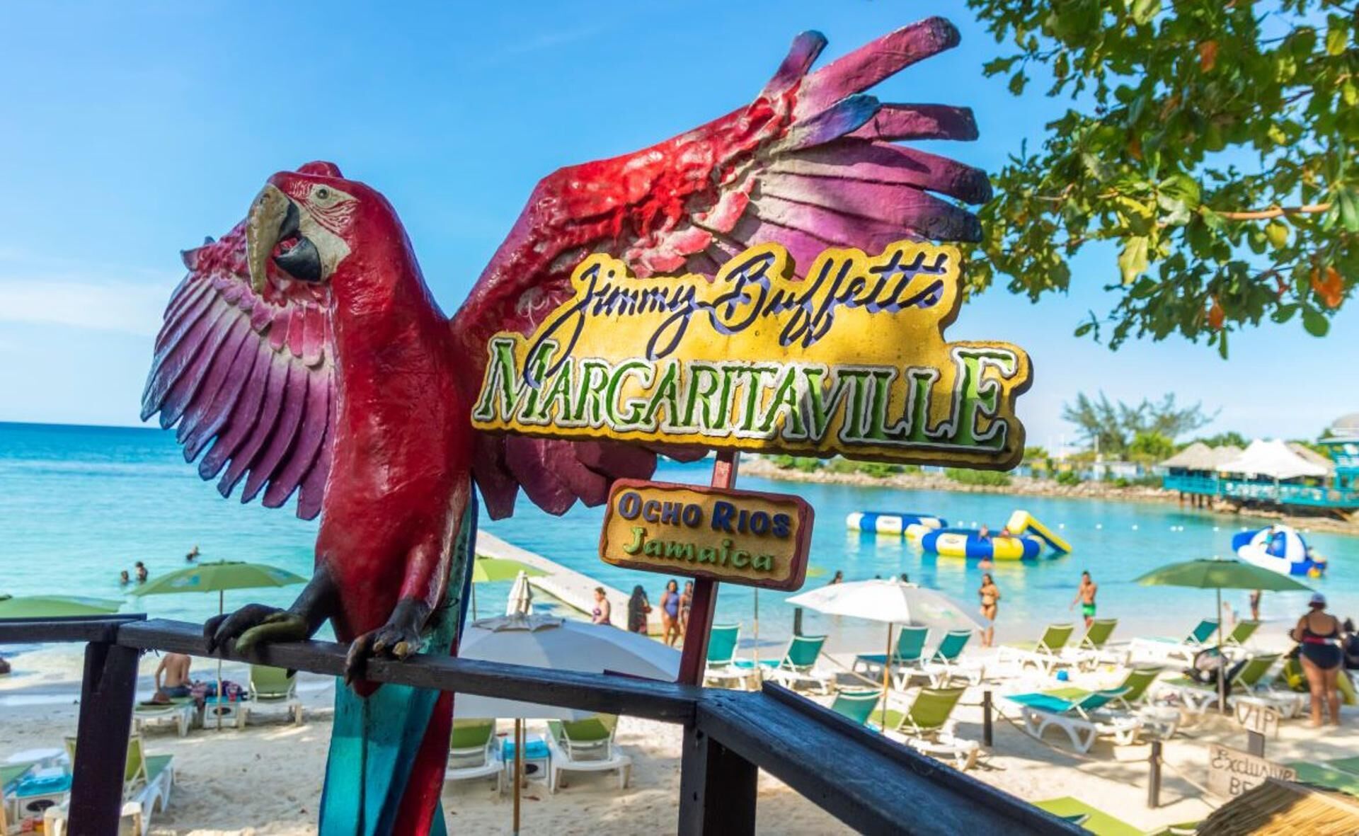 A beach scene with a colorful parrot sign, a pool area, and beach chairs.