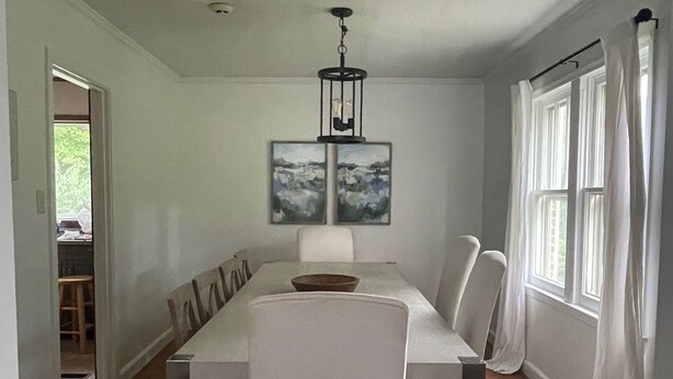 Comedor con mesa rectangular, seis sillas, una araña de techo y dos obras de arte enmarcadas en la pared.