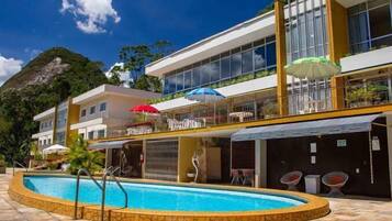 A hotel with a swimming pool, outdoor seating, and a mountain backdrop.