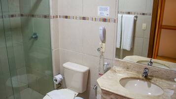 A bathroom with a glass shower enclosure, a toilet, a sink with a mirror, and a towel hanging on the wall.