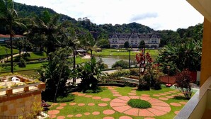 A courtyard with a river view, a large building in the background, and a well-maintained garden with palm trees. - Casa do Sol hotel (Petrópolis)
