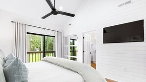 Une chambre à coucher moderne avec un grand lit, des murs blancs, un ventilateur de plafond et une vue sur l’extérieur.