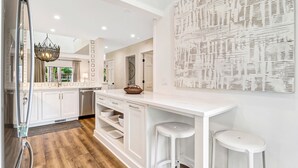 Une cuisine moderne avec des meubles blancs, un îlot central doté de tabourets et un élément décoratif mural.