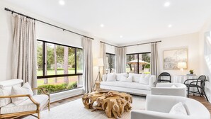 Un salon spacieux avec un canapé blanc, une table basse en bois et une grande fenêtre agrémentée de rideaux.