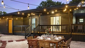An outdoor dining area with a wooden table set for four, surrounded by chairs, and string lights overhead. - Tampa Retreat: 11 Beds, Game Room & Pool! (Tampa)