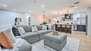 A modern living room with a grey sectional sofa, ottoman, and a dining area with bar stools. - Tampa Retreat: 11 Beds, Game Room & Pool! (Tampa)