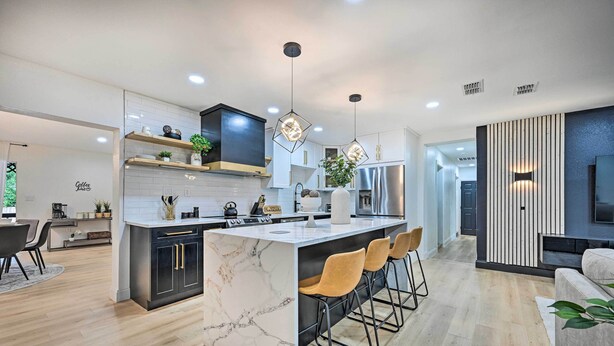 A modern kitchen with marble countertops, a central island with bar stools, pendant lighting, and a built-in oven. - Tampa Retreat: 11 Beds, Game Room & Pool! (Tampa)