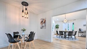A modern dining area with a round table, black chairs, and a hanging light fixture. - Tampa Retreat: 11 Beds, Game Room & Pool! (Tampa)