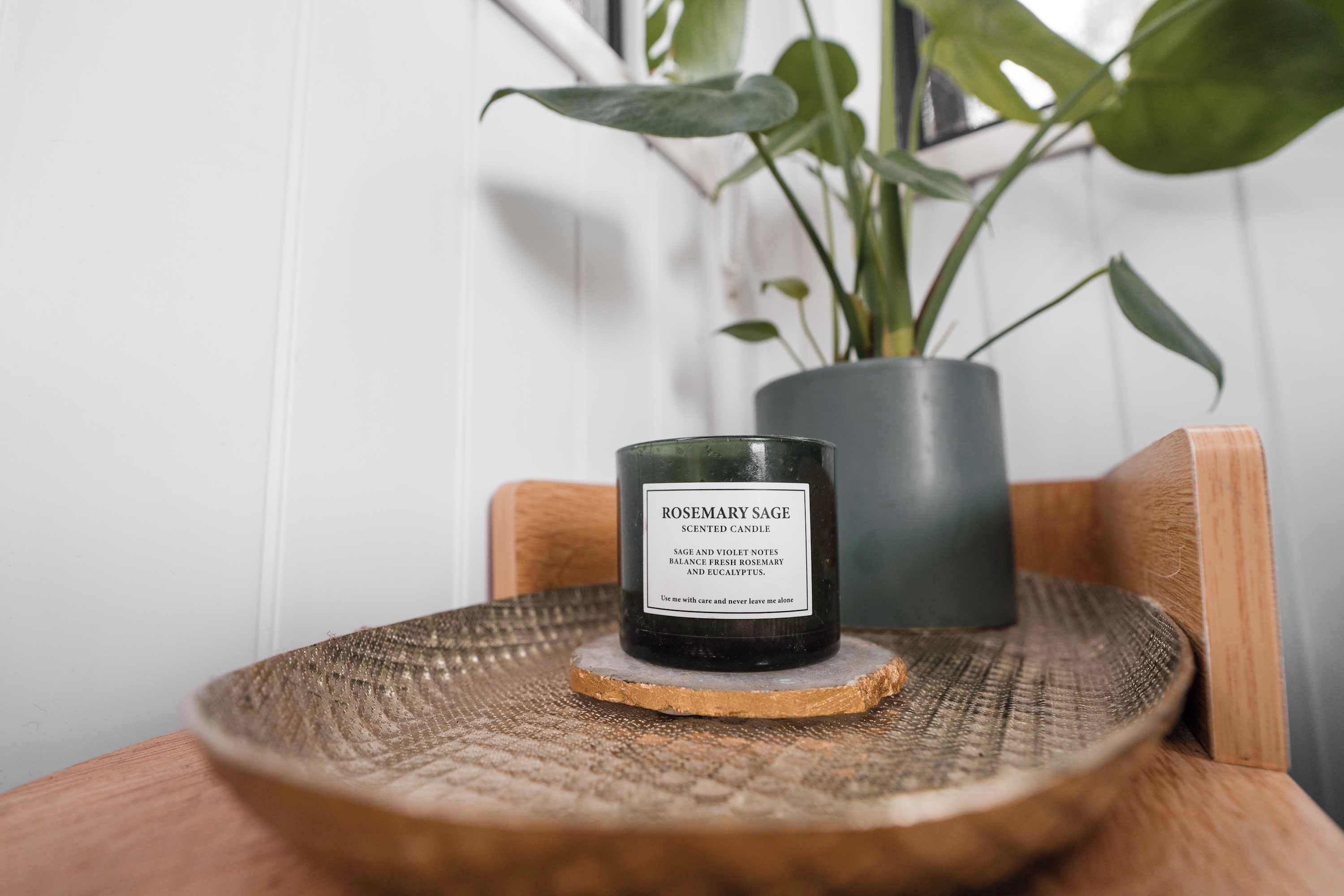 Een geurkaars met de tekst 'ROSEMARY SAGE' op een houten onderzetter.