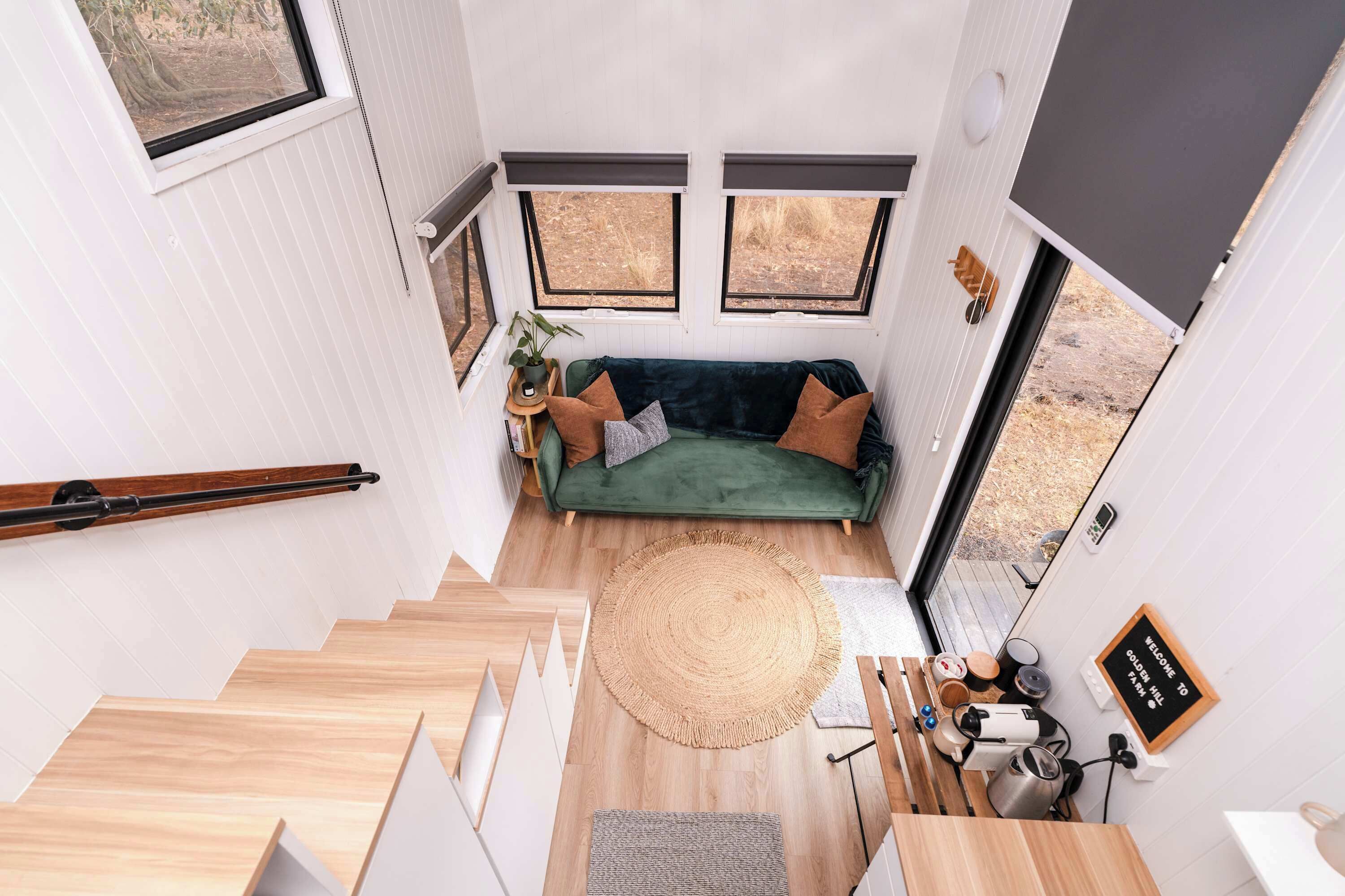 Un espace de vie compact avec un canapé vert, un tapis rond et un escalier menant à un niveau supérieur.
