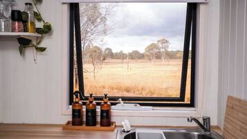 Cucina con vista su un campo, un lavandino e un vassoio di legno con bottiglie.