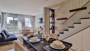 Un comedor moderno con una mesa preparada para cuatro personas, una escalera y una sala de estar con sofá y mesa de comedor.