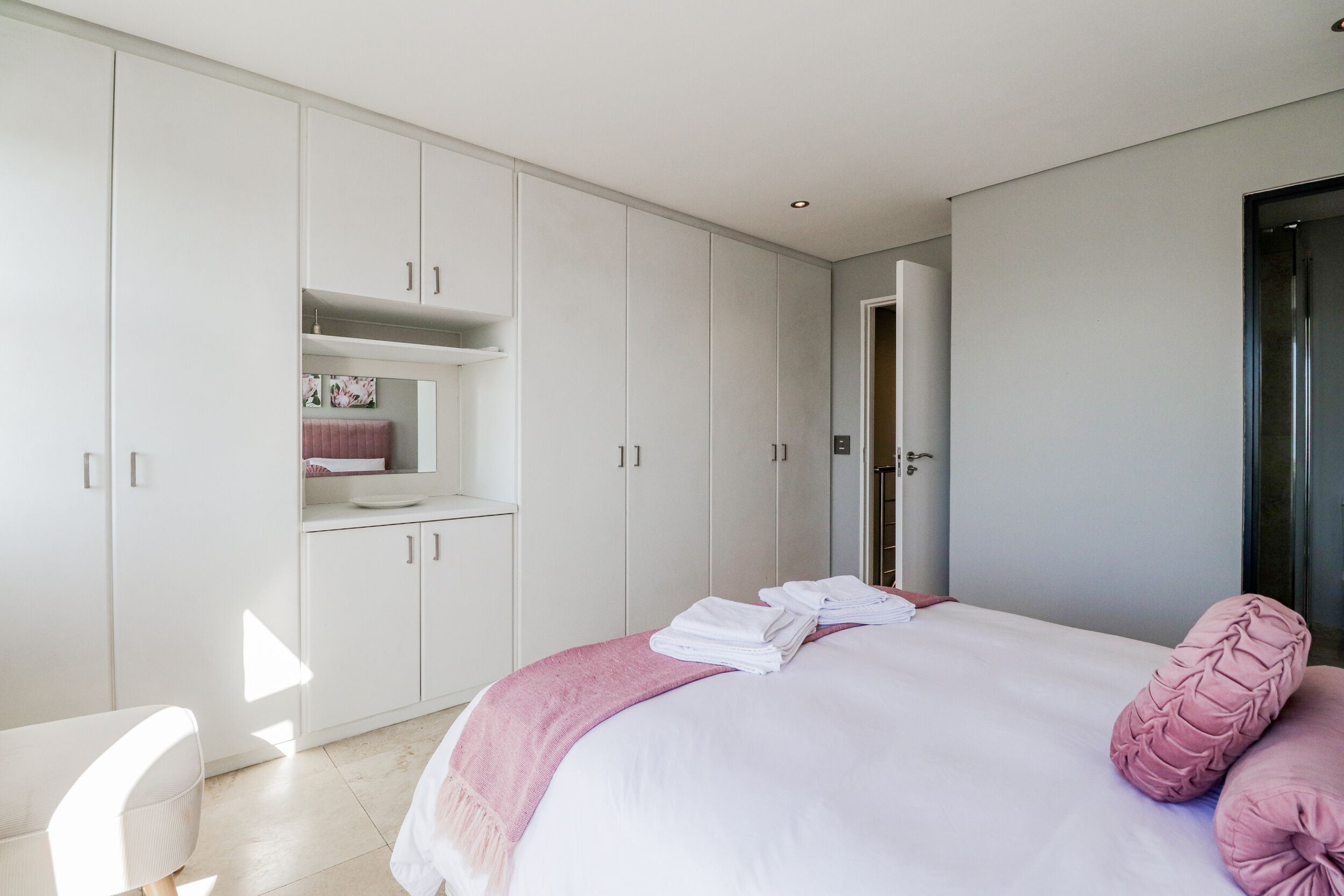 A modern bedroom with a large bed, a built-in wardrobe, and a small seating area.