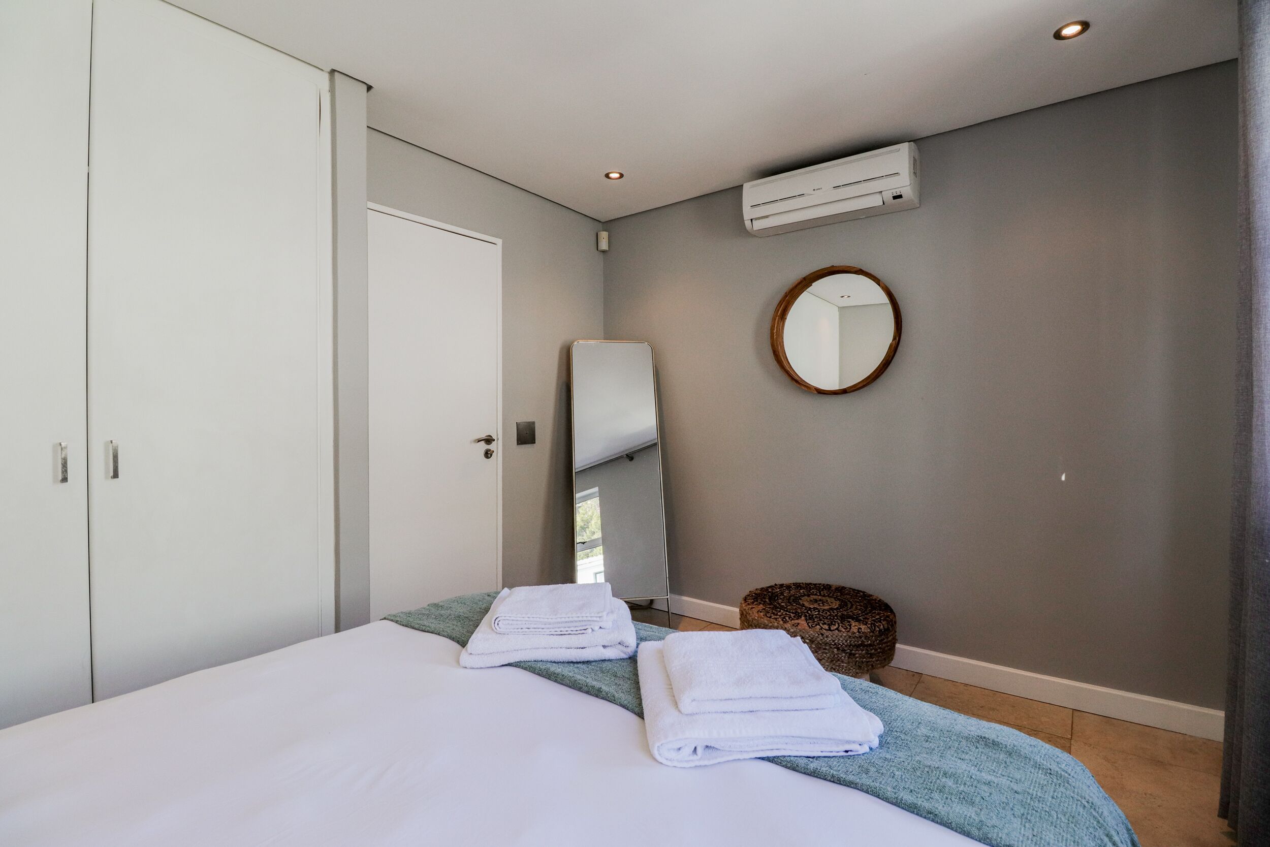 A modern bedroom with a bed, white towels, a round mirror, and a small round table.