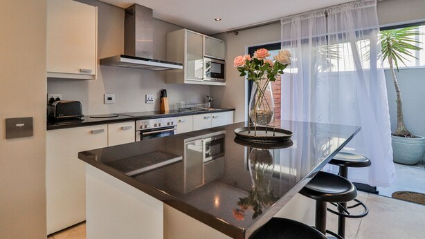 Una cocina moderna con una isla central, electrodomésticos integrados y un amplio ventanal con cortinas translúcidas.