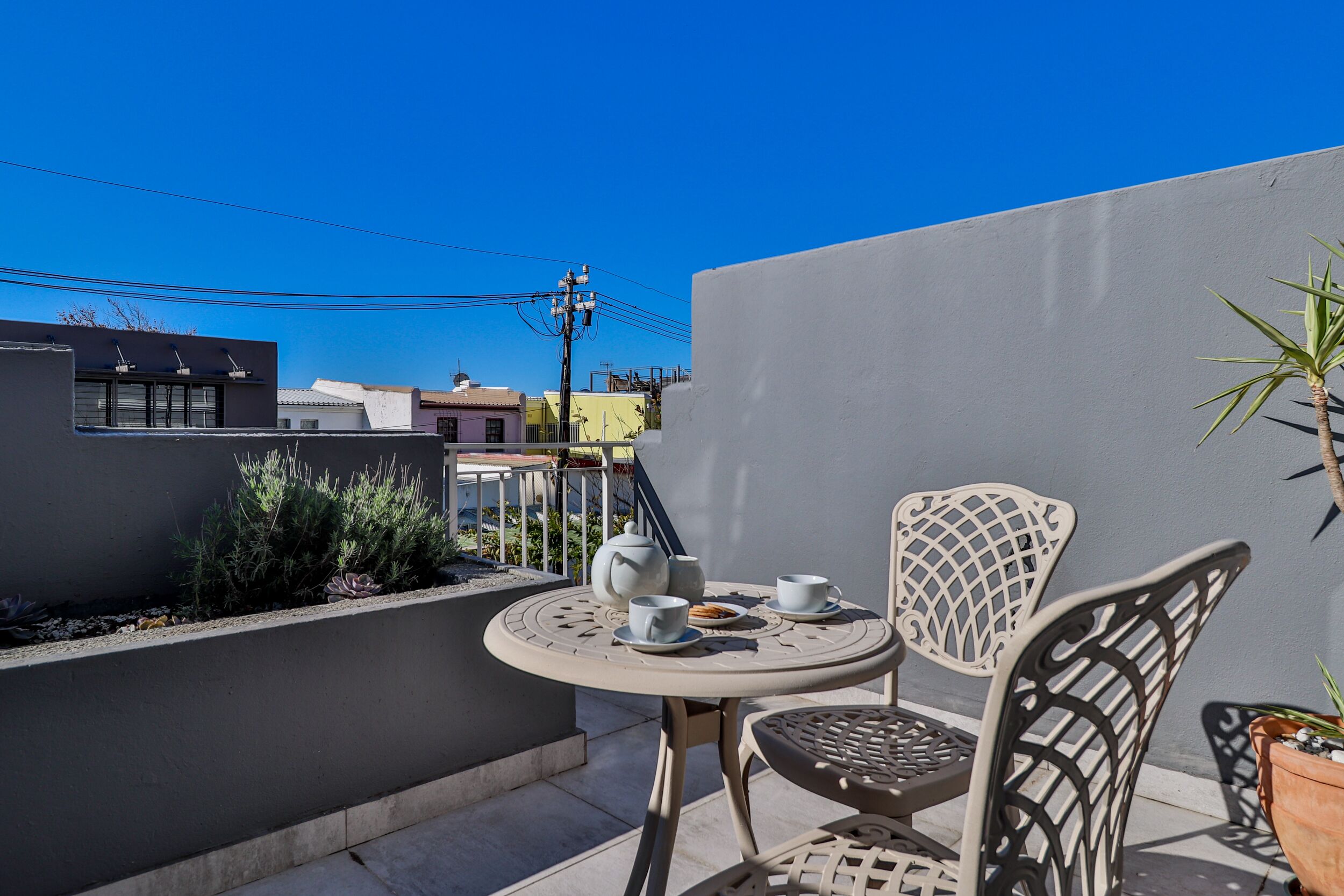 A small outdoor seating area with a round table and two chairs, a potted plant, and a view of the surrounding buildings.