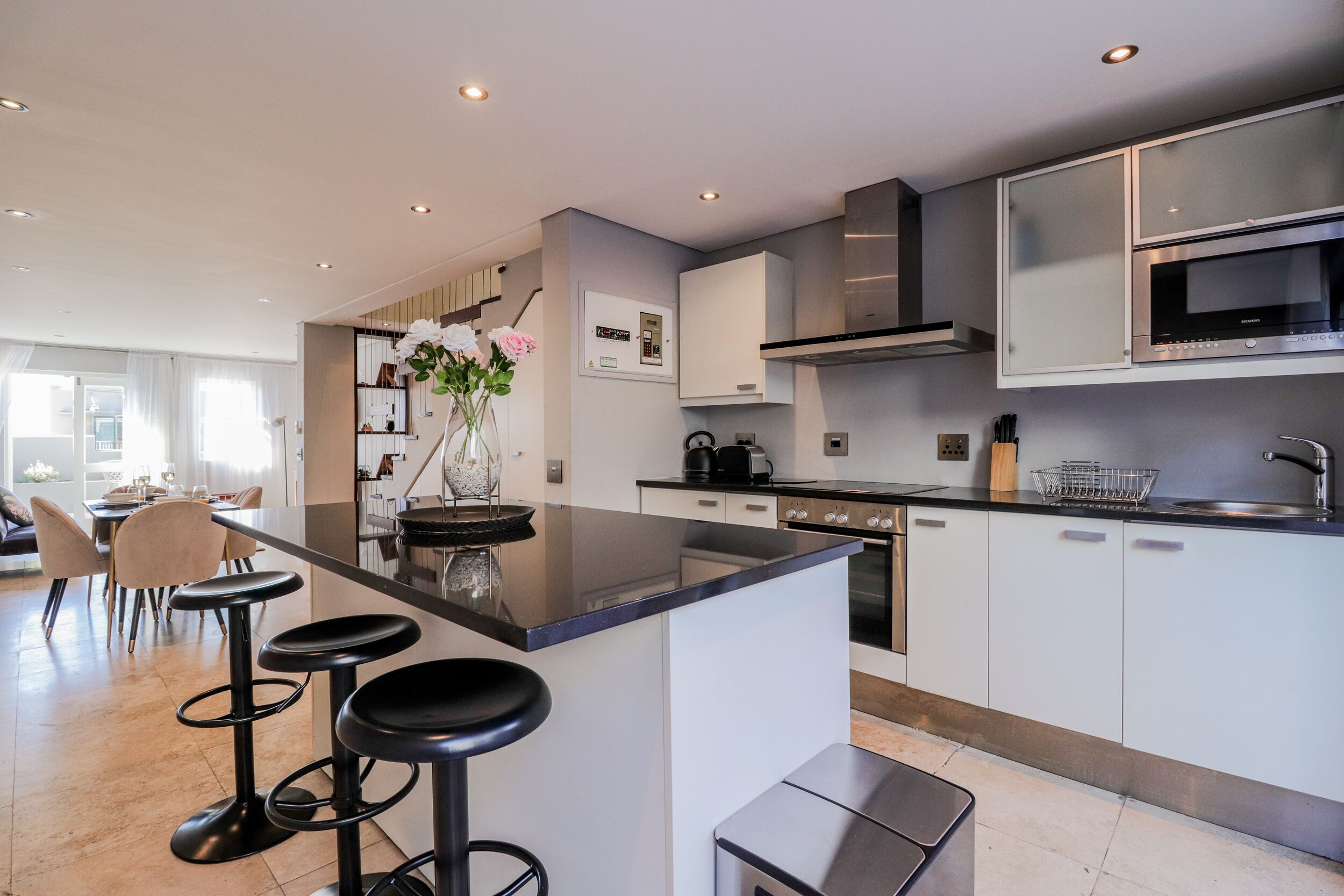 Een moderne keuken met een centraal eiland, barkrukken en roestvrijstalen apparatuur.
