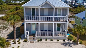 Une maison de plage à deux étages, dotée d’un balcon à chaque niveau, d’un porche à l’avant et d’un petit jardin.