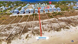 Vue aérienne d’une zone résidentielle côtière, avec des maisons, un chemin balisé menant à la plage et une vue sur l’océan.