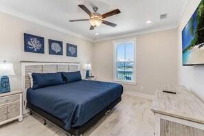 A bedroom with a bed, nightstands, a ceiling fan, artwork, and a view of the outdoors. - Cape San Blas Beach House | Pool & Pickleball | Beach Access (Port St Joe)