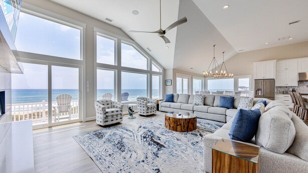 A spacious living room with a large view of the ocean, a ceiling fan, and a modern kitchen area.