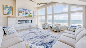 A spacious living room with a large window overlooking the ocean, a fireplace, and a modern ceiling fan.
