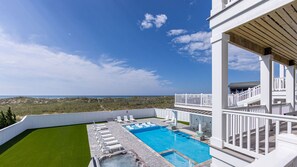 A pool area with a view of the ocean, a grassy area, and a white building with a balcony. - Premier Oceanfront Estate w/ Pool, Hot Tubs, Elevator, Theater, and Much More (Hatteras)