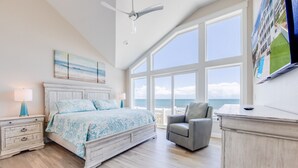 A bedroom with a large bed, a chair, a dresser, and a view of the ocean.