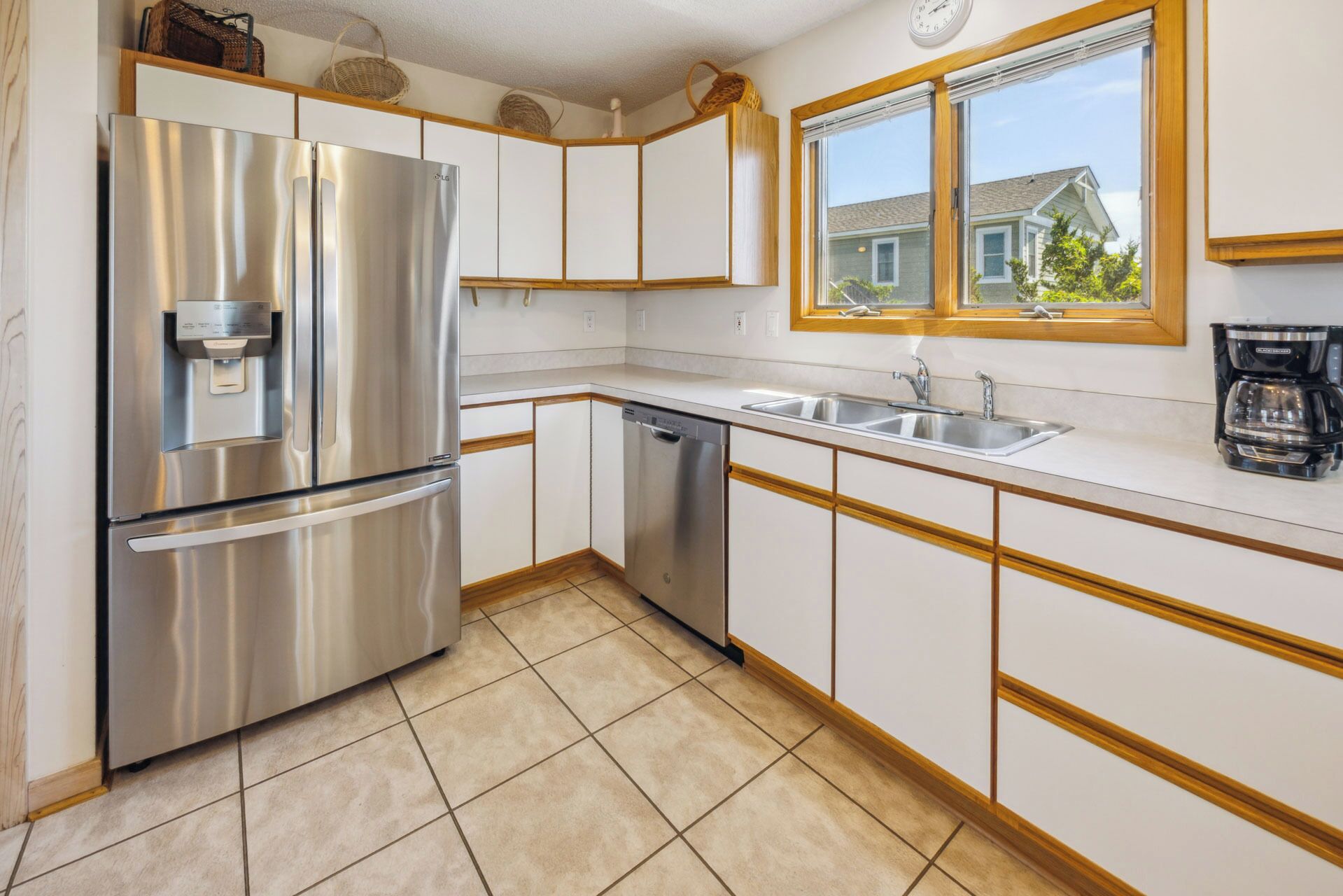 Una cocina con un refrigerador de acero inoxidable, lavavajillas y una ventana que ofrece vistas a una casa.