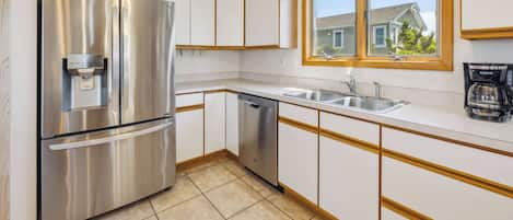 Una cocina con un refrigerador de acero inoxidable, lavavajillas y una ventana que ofrece vistas a una casa.