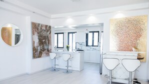 A modern kitchen with white cabinetry, a marble countertop, and two bar stools. - Luxury Apt in the center of Glyfada (Glyfada)
