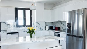 A modern kitchen with white cabinets, a marble countertop, a stainless steel refrigerator, and a central island with chairs. - Luxury Apt in the center of Glyfada (Glyfada)