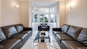 A spacious living room with two leather sofas, a coffee table, and a bay window with stained glass. - Delightful Holiday Home With sea Views and Hot Tub (Penmaenmawr)