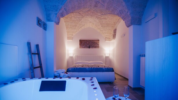 Een slaapkamer met een stenen plafond, een bed met rozenblaadjes en een nachtkastje met een glas wijn.
