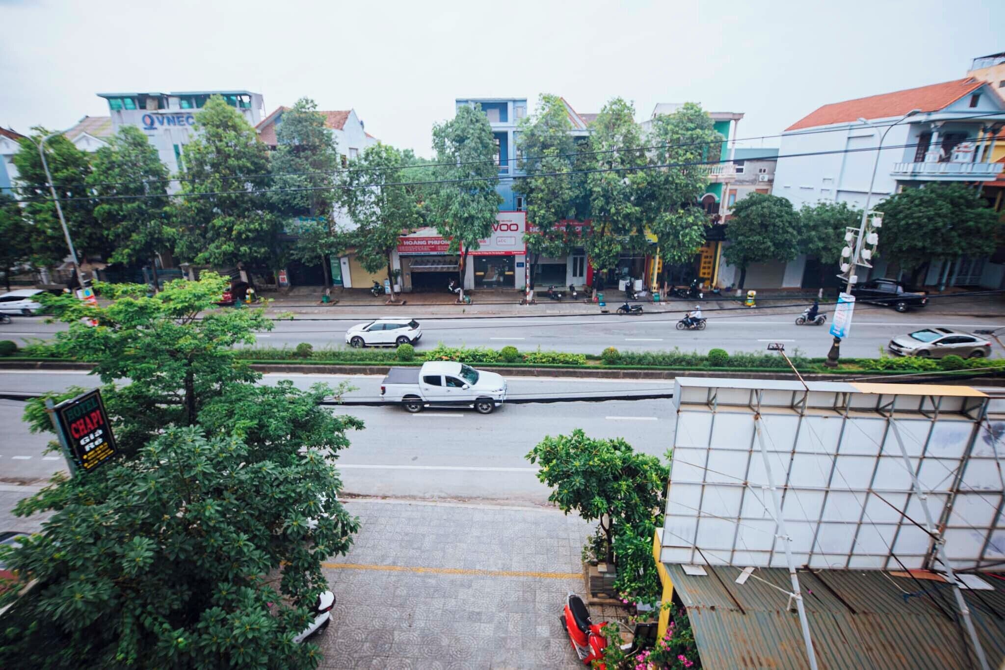 A street view with buildings, trees, and parked vehicles.