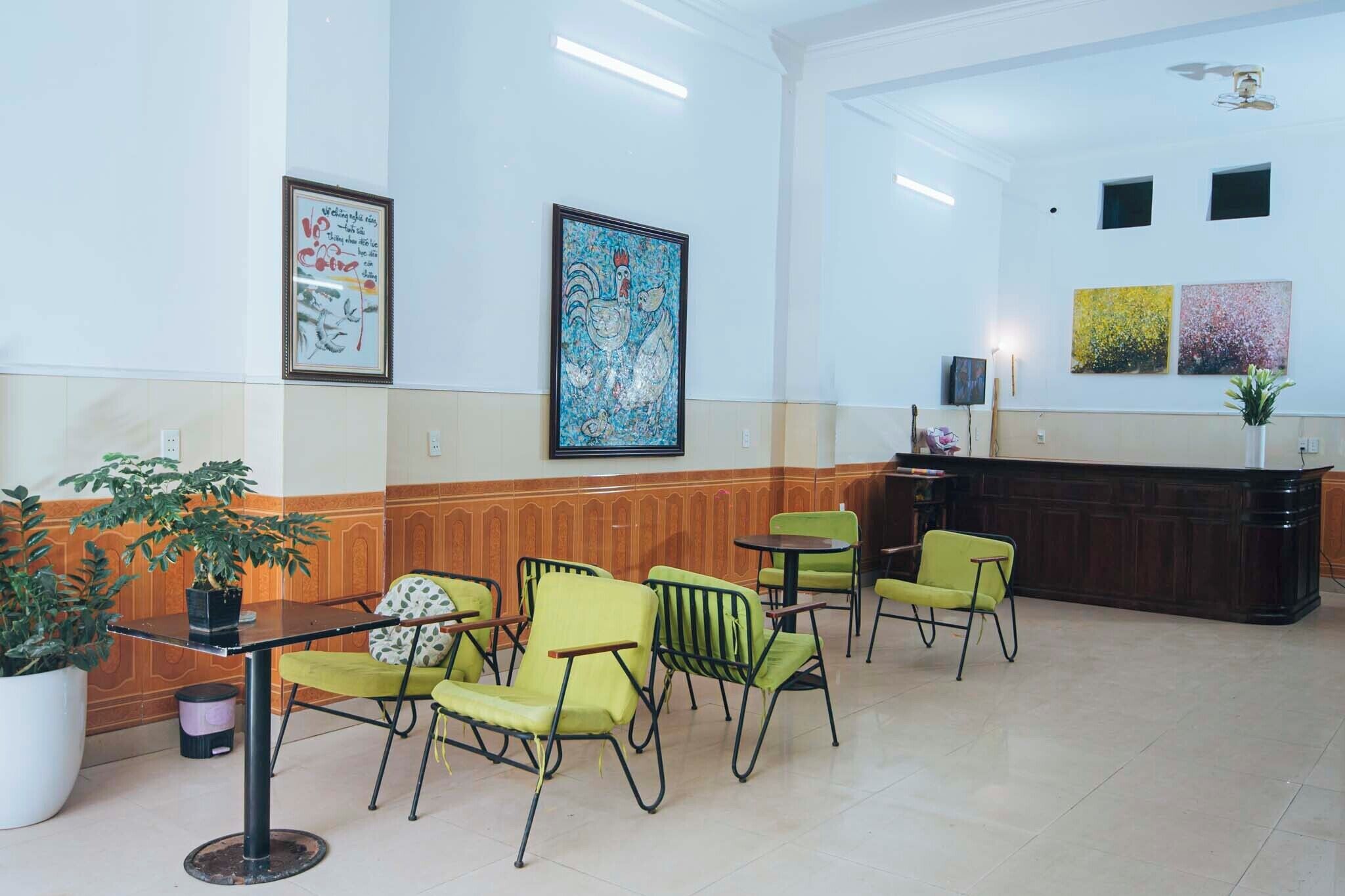 A lobby with a reception desk, green chairs, a potted plant, and artwork on the walls.
