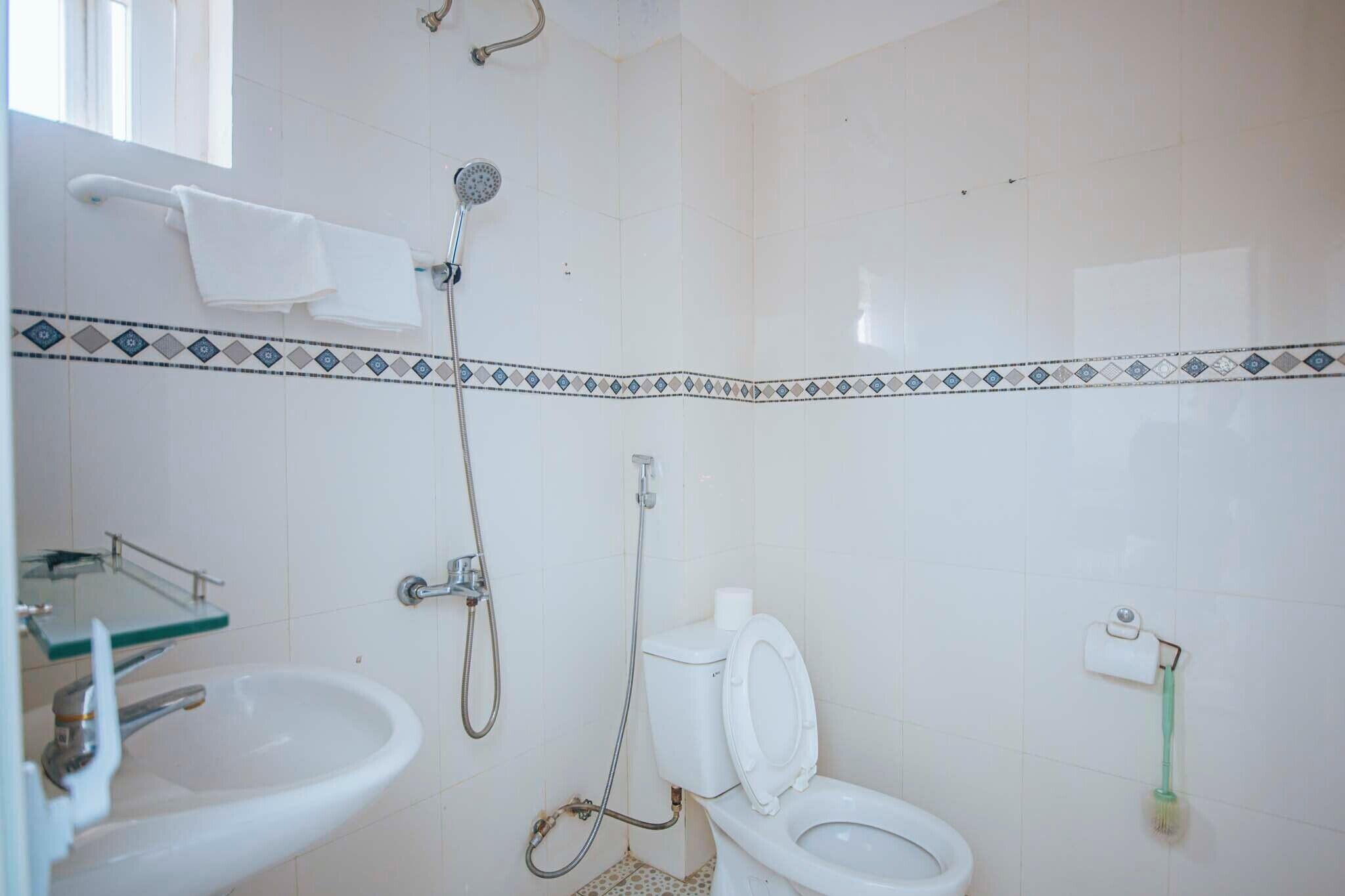 Un baño con ducha, inodoro, lavamanos y un perchero para toallas.