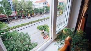 A view from a window overlooking a street with buildings, trees, and a red scooter parked on the sidewalk. - Chapi Hotel (Dong Hoi)