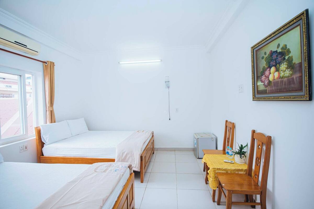 Una habitación con dos camas, una mesa con sillas, un cuadro y una ventana.