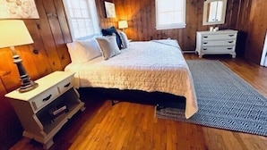 A wooden-paneled bedroom with a bed, nightstands, a dresser, and a window. - Cabin 5 - Rustic cabin in Pioneer Village, Great Smoky Mountains NC (Maggie Valley)