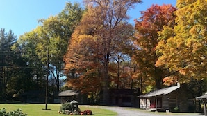 A rustic cabin with a stone exterior, surrounded by a well-maintained lawn and autumn-colored trees. - Cabin 5 - Rustic cabin in Pioneer Village, Great Smoky Mountains NC (Maggie Valley)