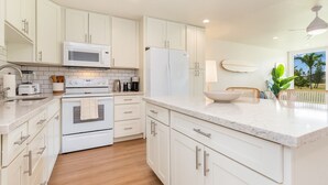 A modern kitchen with white cabinets, a microwave, a refrigerator, a stove, and a sink. - Hale Maluhia ~ Peaceful home (Kawela Bay)